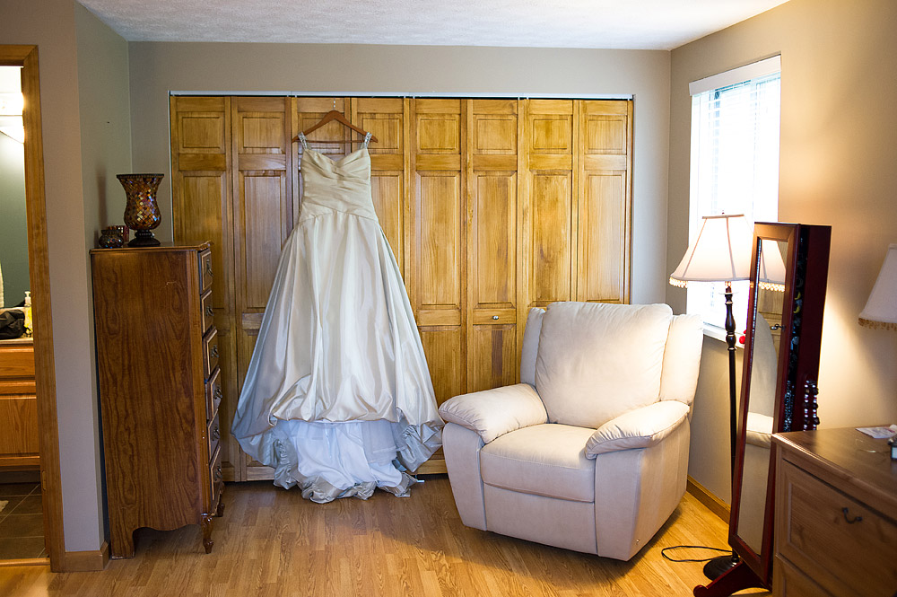 White wedding dress hanging before wooden bedroom doors