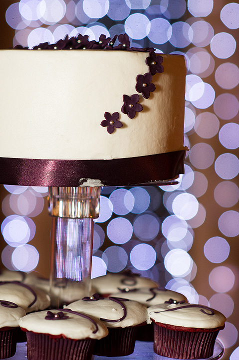 White wedding cake with purple ribbon and matching cupcakes