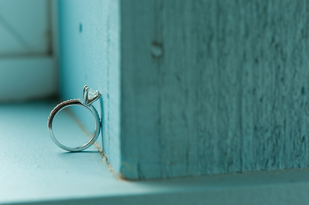 Diamond engagement ring and band balanced on the edge of a teal box