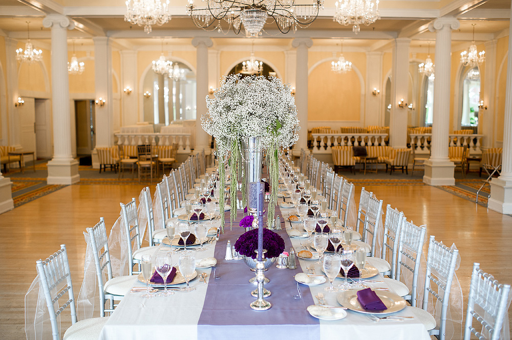 Reception table with purple linens and a tall white floral centerpiece