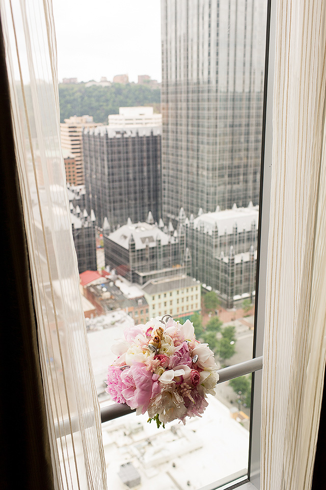 Pink bridal bouquet beside a hotel window overlooking Pittsburgh