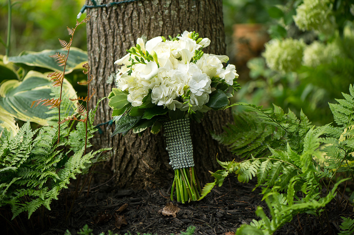 White bridal bouquet with greenery resting against a tree