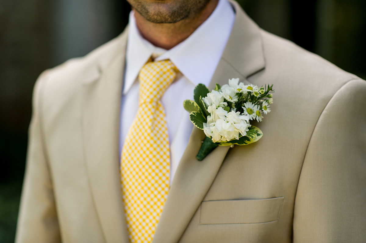 Tan wedding suit with a yellow patterned tie and white boutonniere