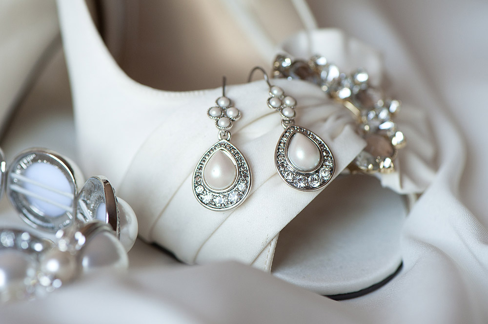 Silver bridal jewelry and earrings arranged on a white high heel