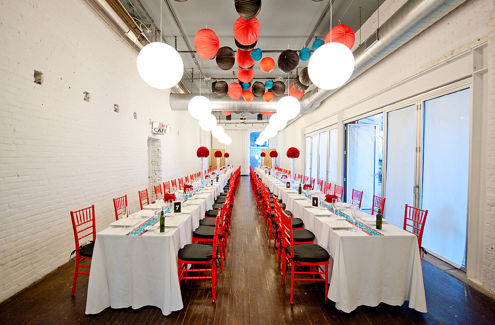 Long reception tables with red chairs and hanging lanterns