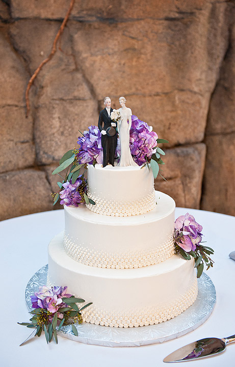Three-tier white wedding cake with purple flowers and a couple topper