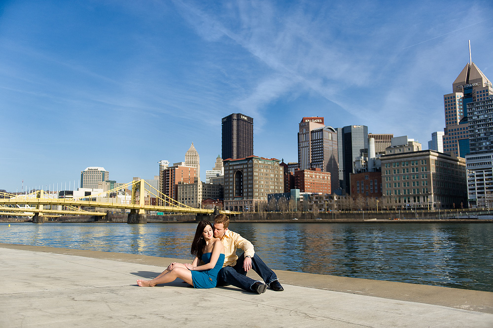 Couple seated along the Pittsburgh riverfront with the skyline and bridge behind them