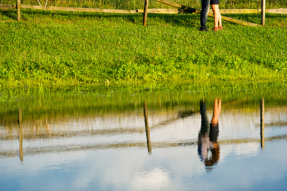 Couple reflected in a pond while standing on the grassy bank