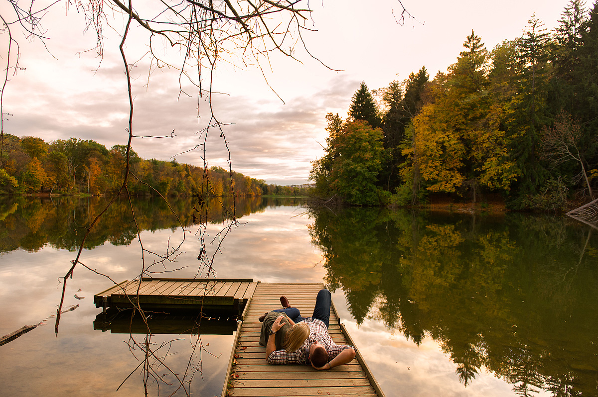 Couple seated together on a dock beside an autumn lake