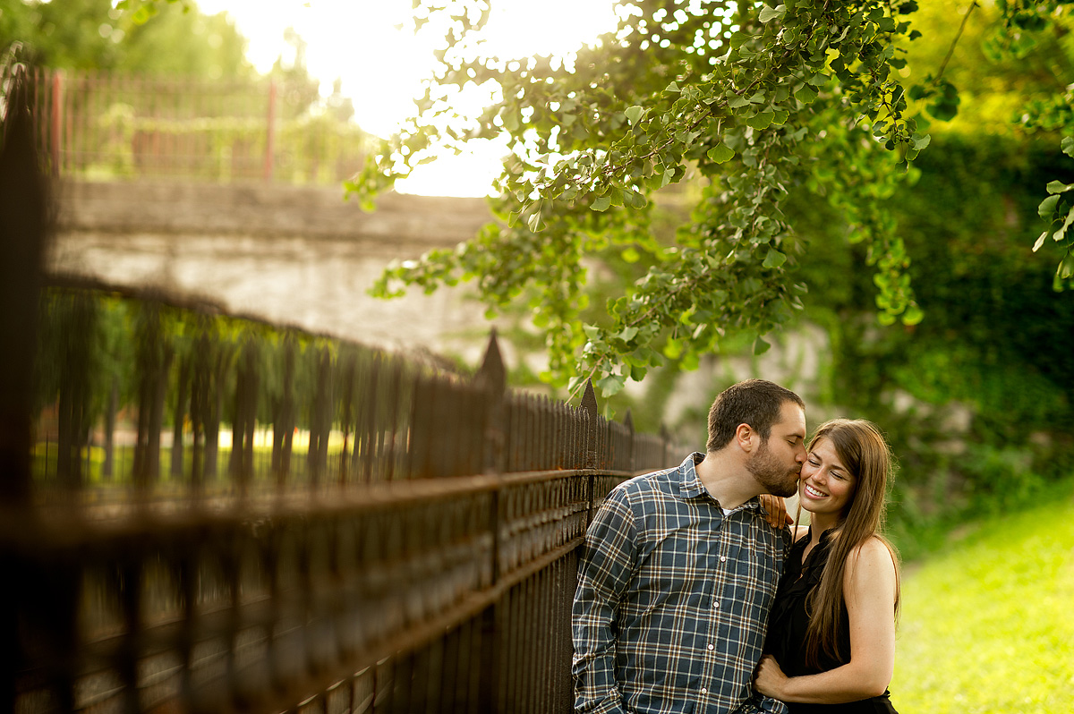 Couple kissing beside a park fence at golden hour
