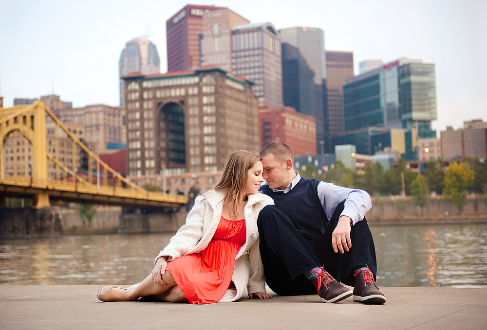 Couple seated on the riverfront with the Pittsburgh skyline and a yellow bridge behind them