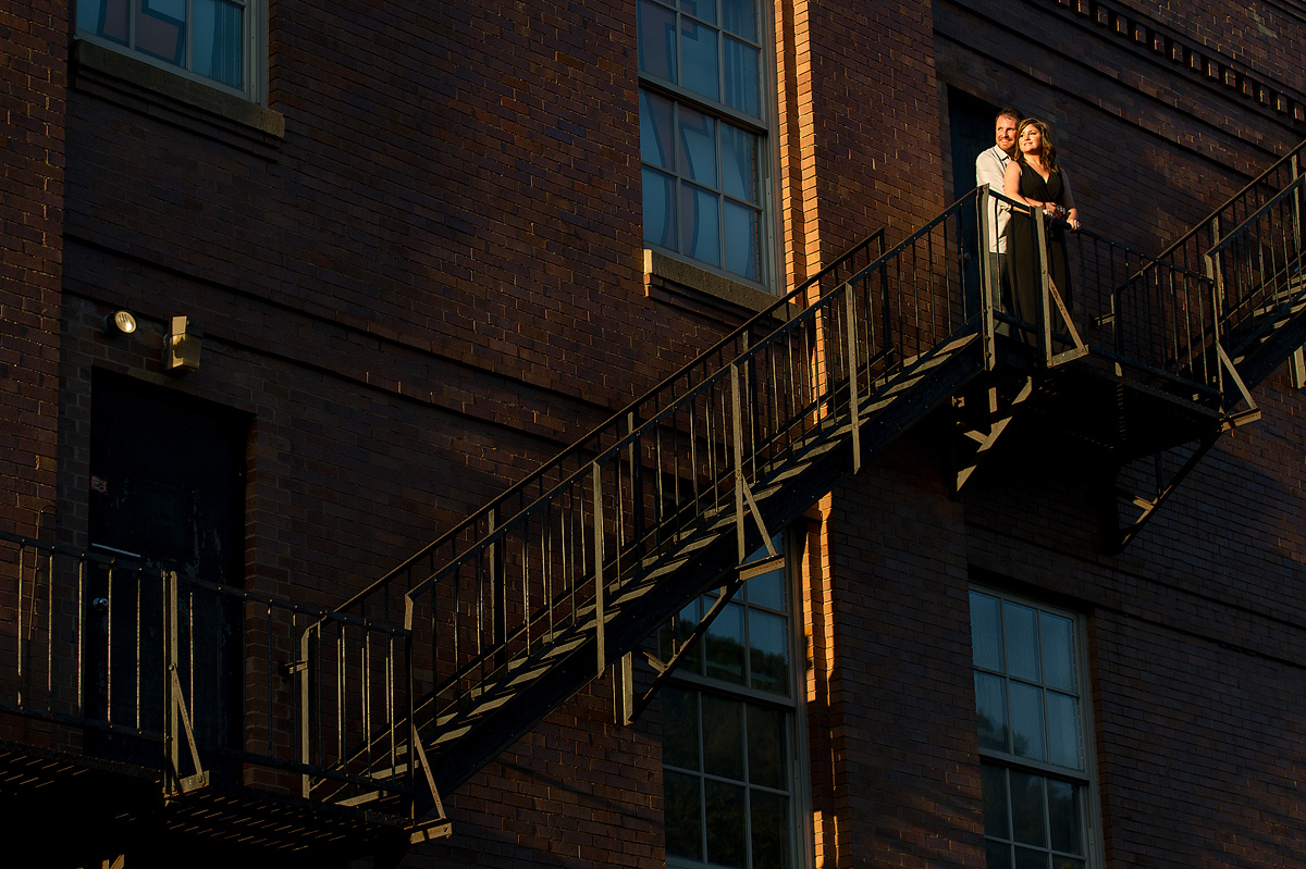 Couple on an exterior metal staircase of a brick building at sunset