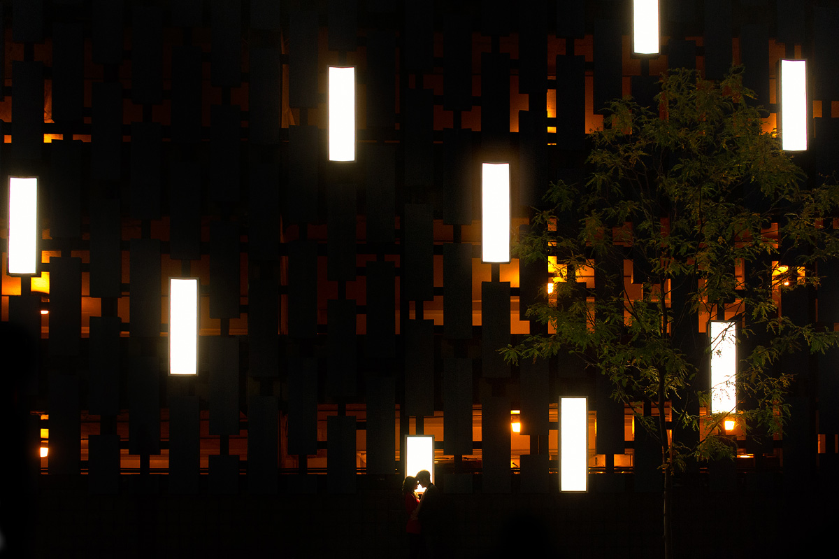 Couple silhouetted before an illuminated geometric wall at night