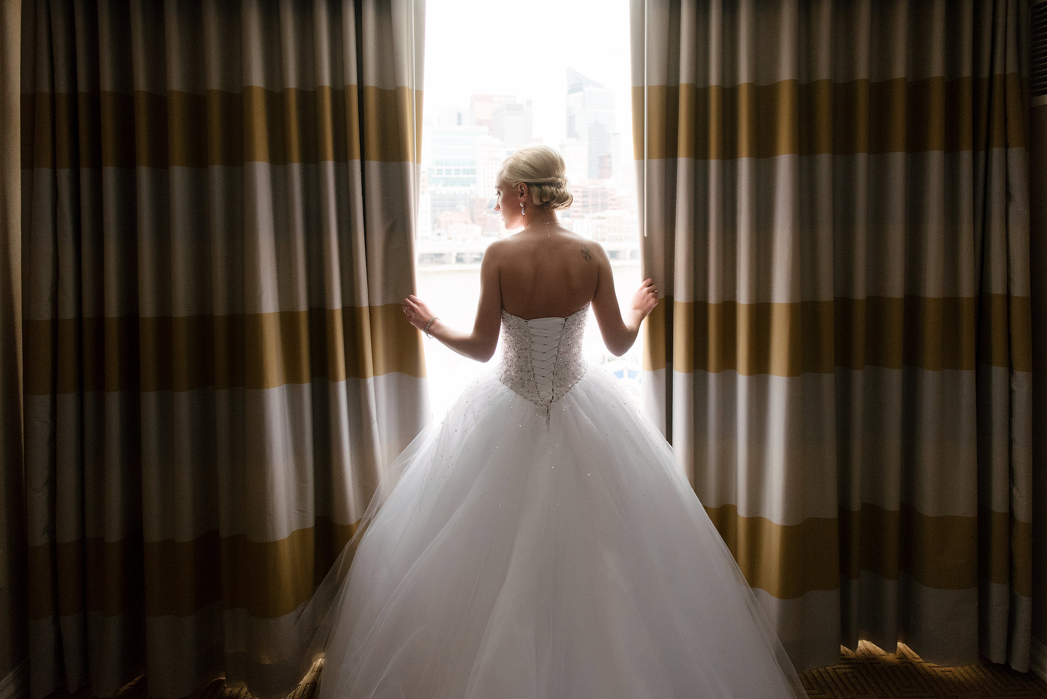Bride opening striped curtains in her wedding dress
