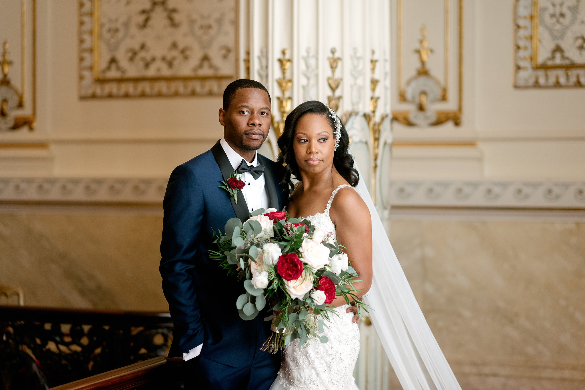 Bride and groom holding a red-and-white bouquet inside Heinz Hall