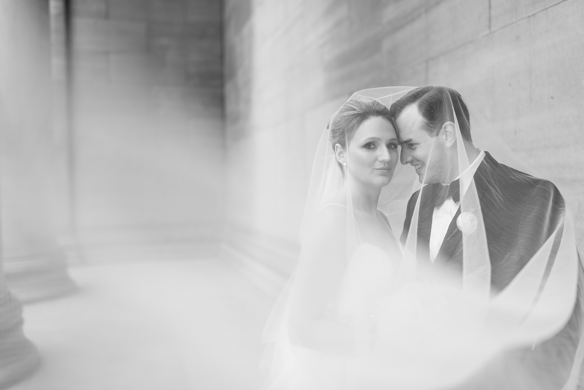 Black-and-white double-exposure portrait of newlyweds beneath the bride's veil