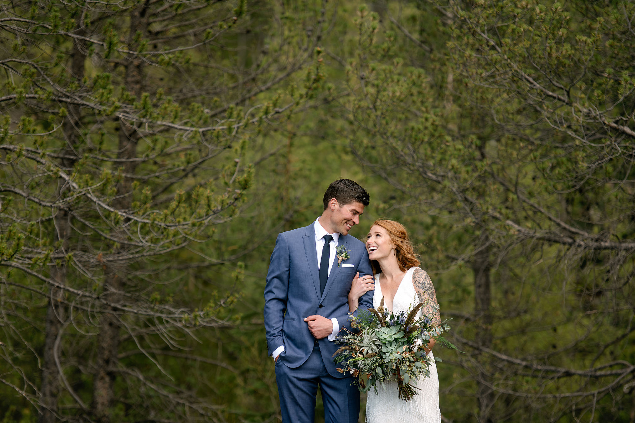 Wedding couple holding a greenery bouquet among Colorado evergreens
