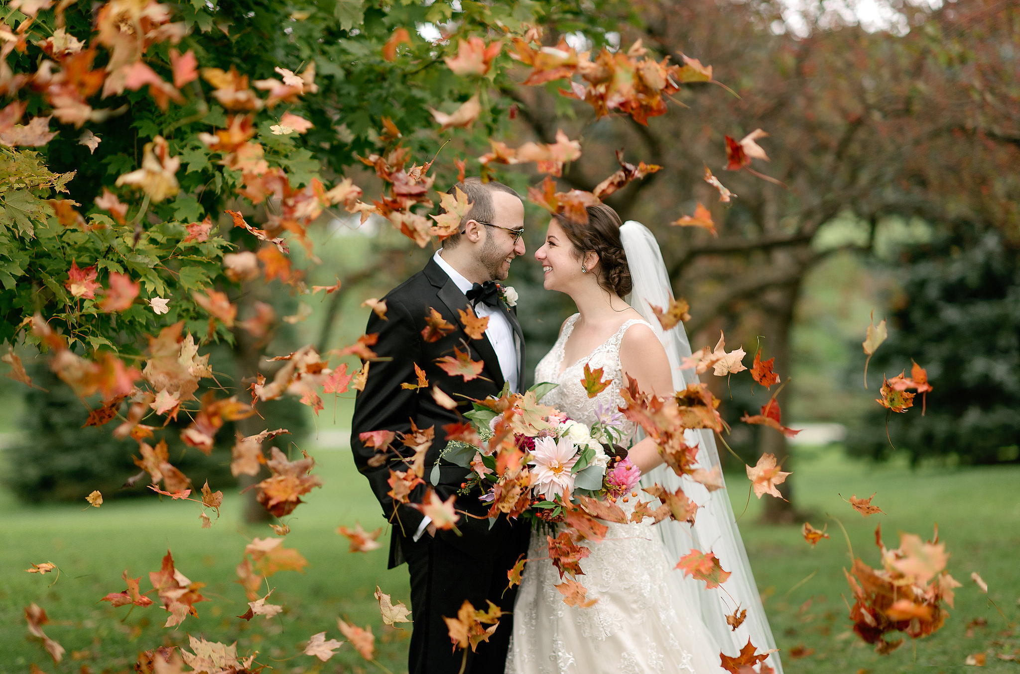 Newlyweds kissing as autumn leaves swirl around them
