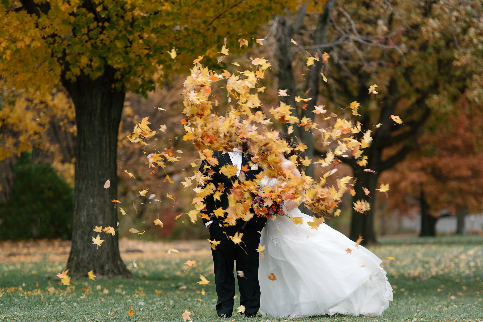 Smiling newlyweds as autumn leaves fly around them