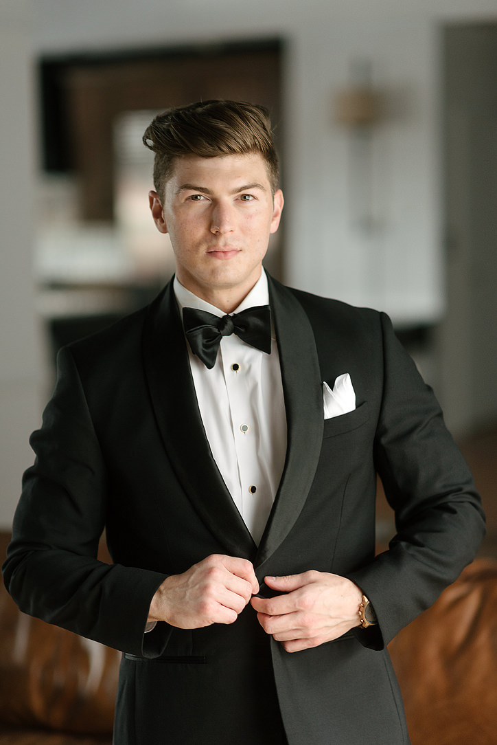 Groom adjusting his tuxedo jacket