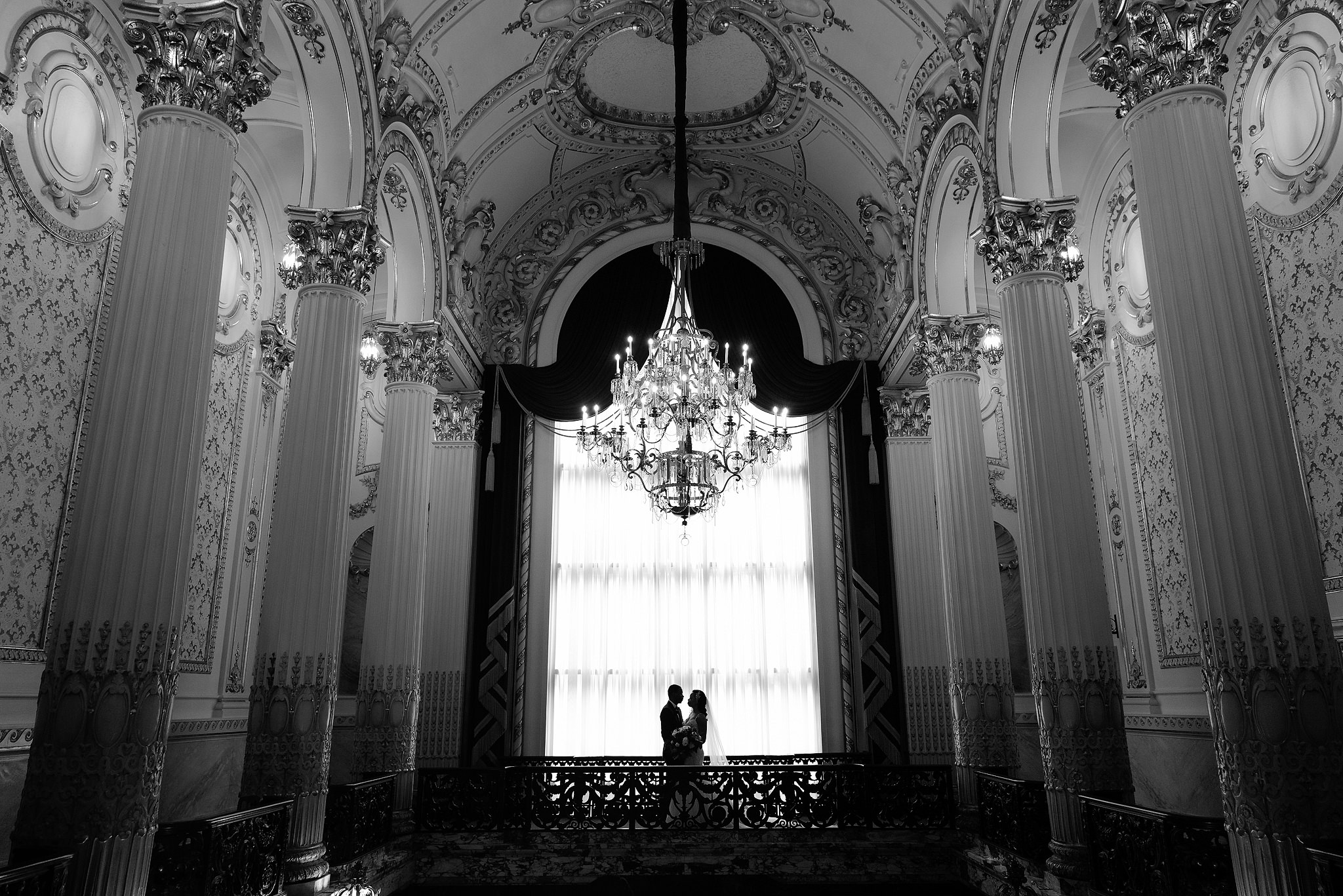 Wedding couple silhouetted beneath a chandelier inside Heinz Hall
