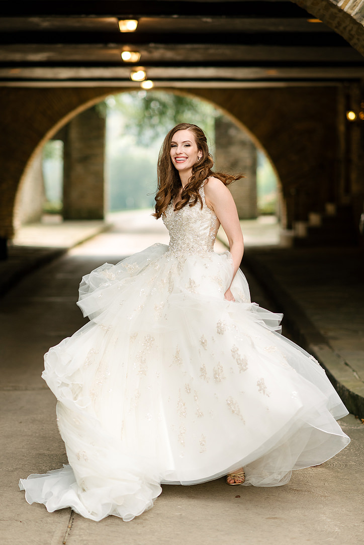 Bride walking in a full ball gown beneath a stone arch at Longue Vue Club