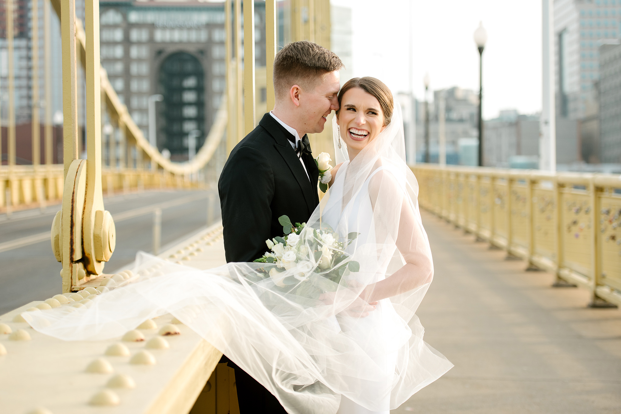 Newlyweds on a yellow Pittsburgh bridge with the bride's veil flowing