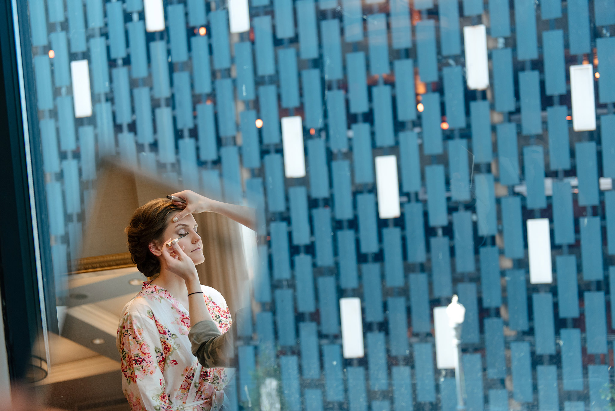 Bride beside a blue geometric wall with the groom reflected behind her