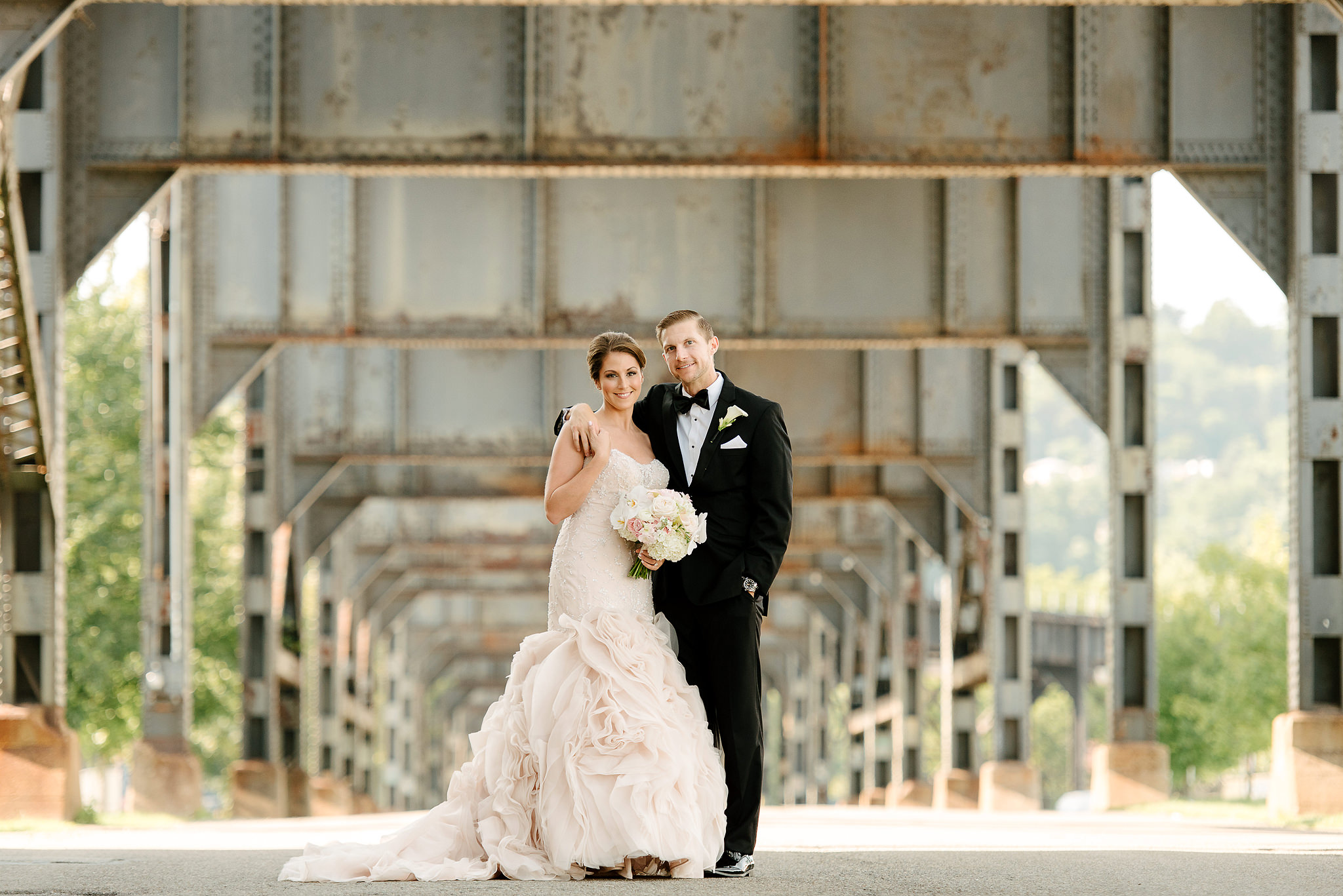 Bride and groom beneath an industrial steel structure in Pittsburgh's Strip District