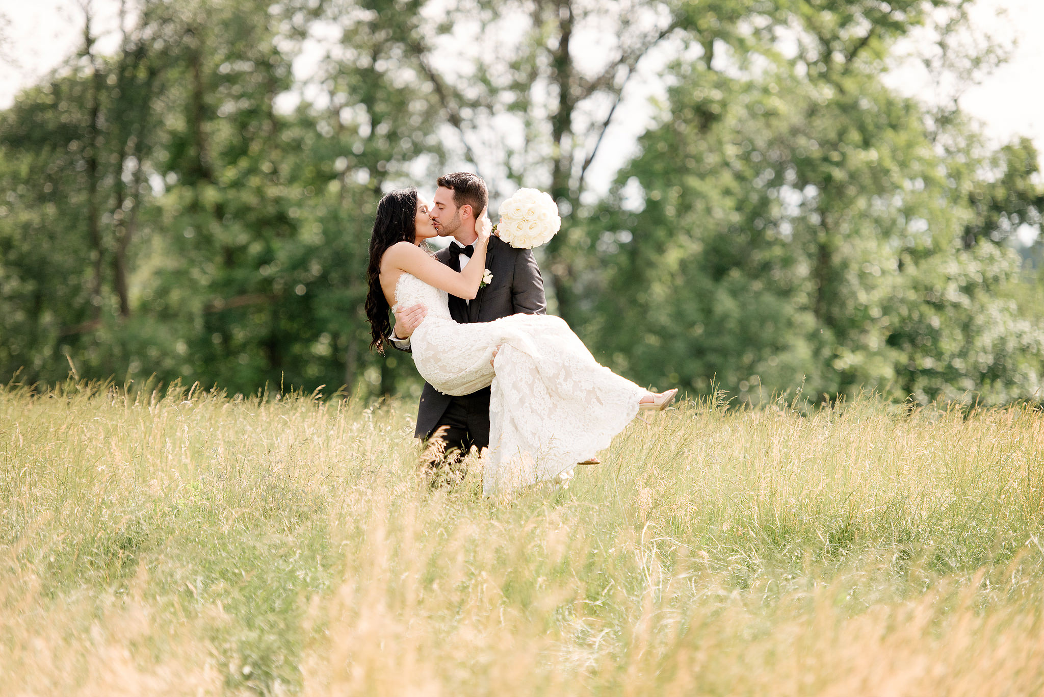 Groom lifting the bride in a sunlit meadow at Longue Vue Club