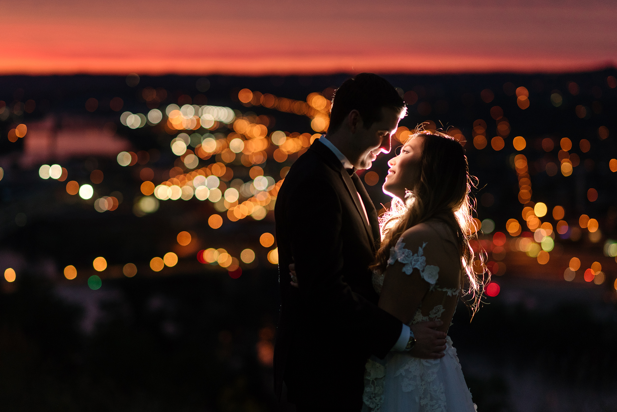 Newlyweds kissing beneath warm string lights at sunset