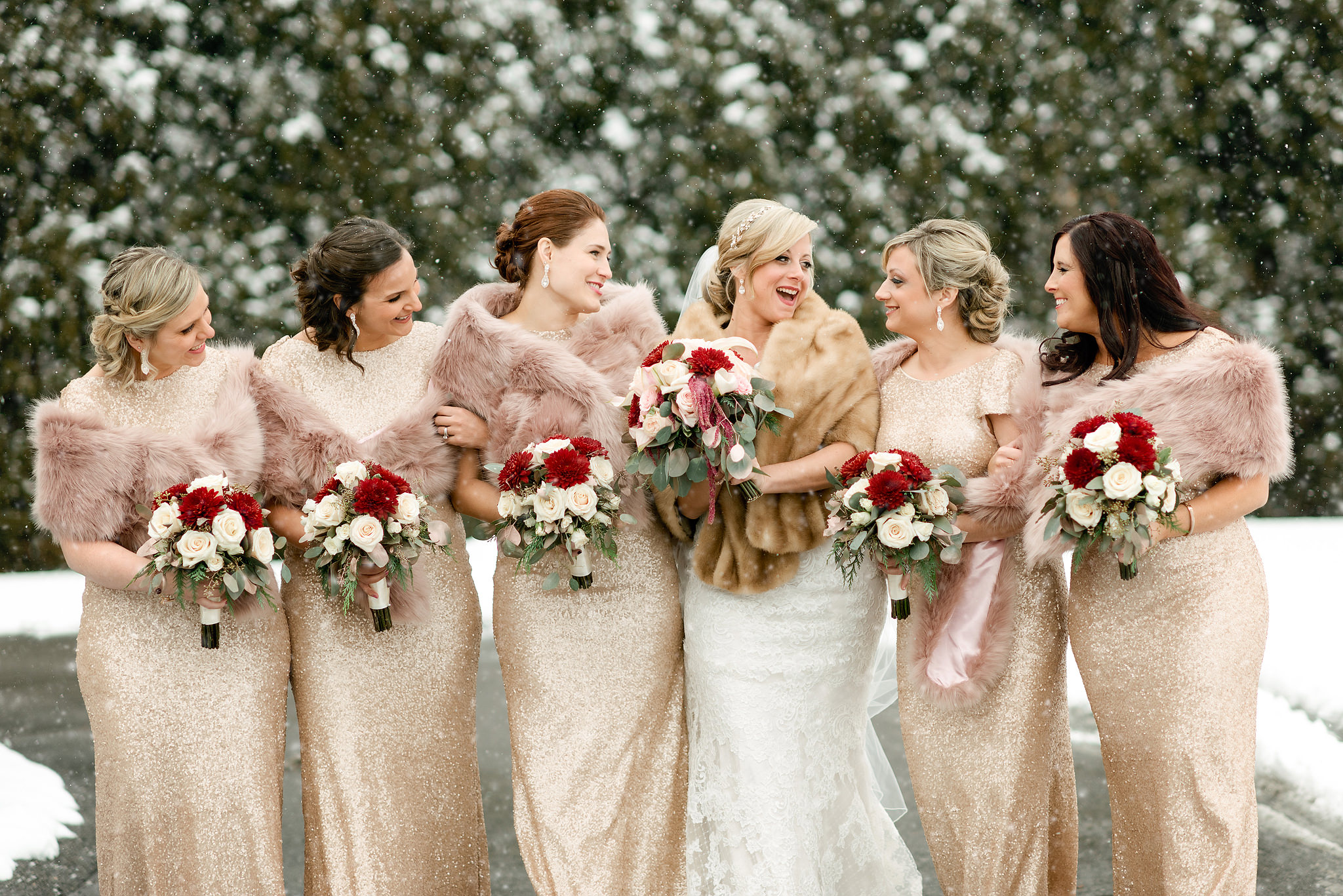 Bride with bridesmaids in falling snow holding red bouquets